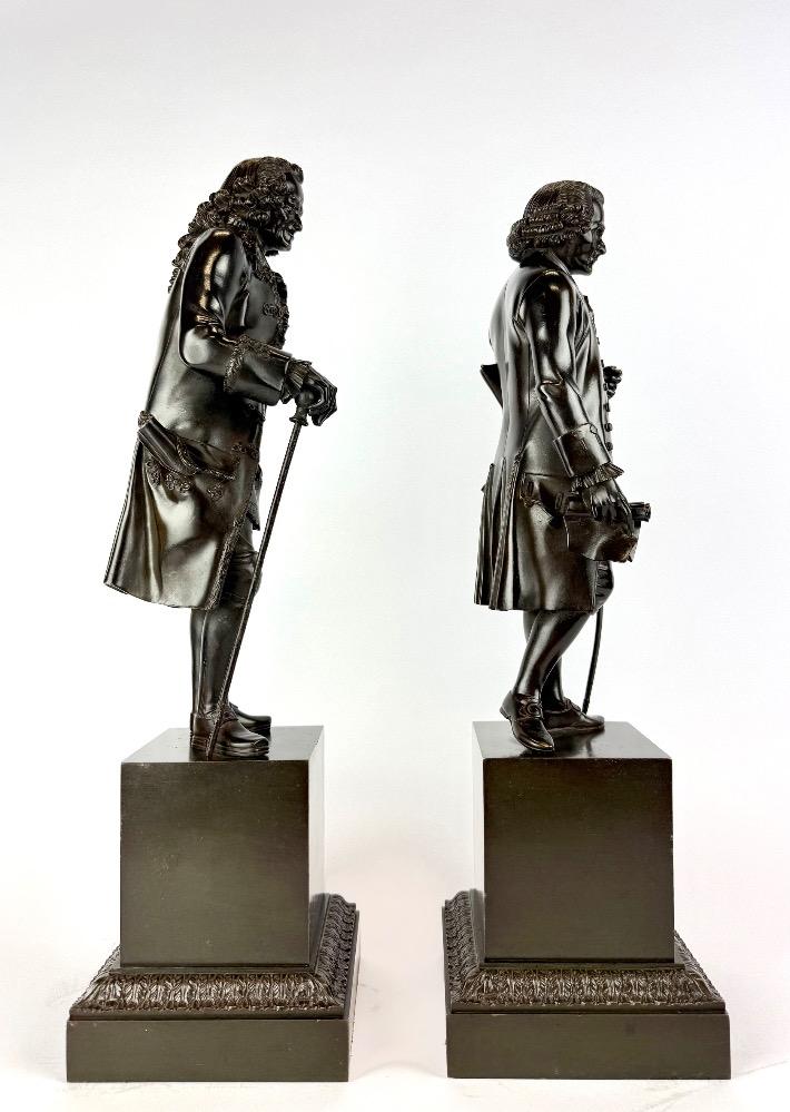 A pair of bronze sculptures of Voltaire and Rousseau.